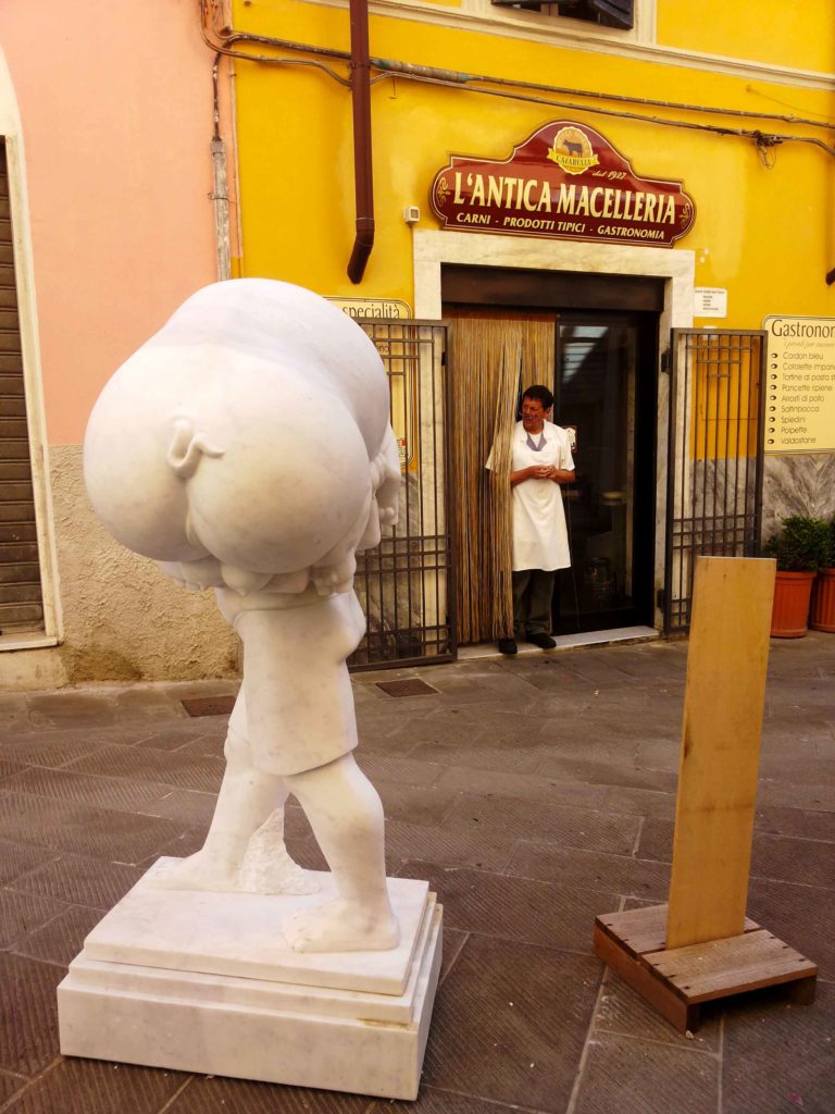 scultura in marmo raffigurante un maiale, di fronte a una macelleria